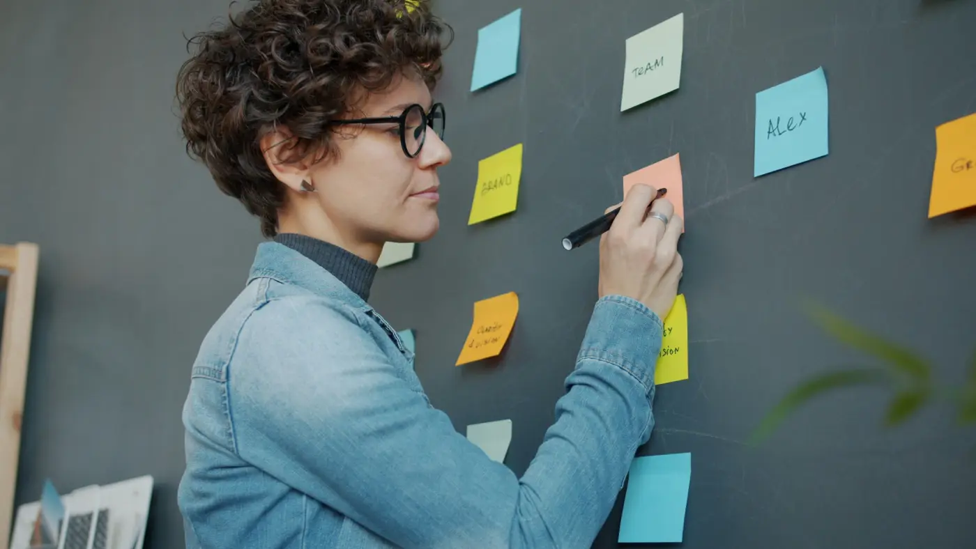 A woman writing on coloured sticky notes on a dark wall